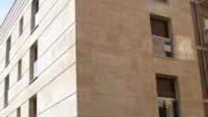 Un edificio de varios pisos con fachada plana y ventanas rectangulares. Dos coches estacionados en la parte delantera.