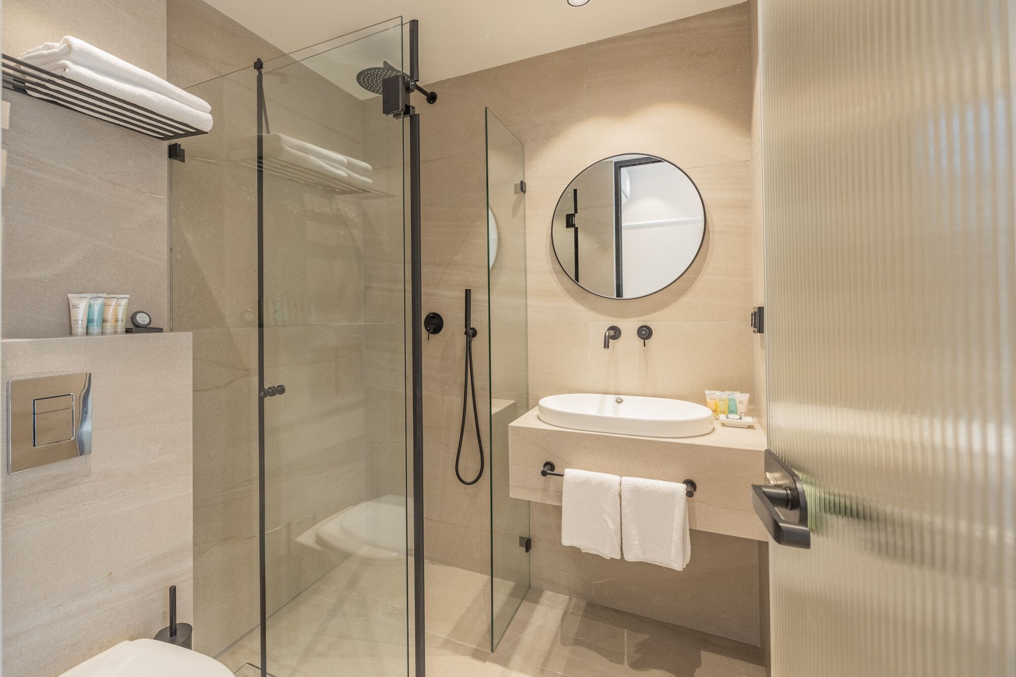 Un baño moderno con ducha de vidrio, espejo redondo, lavamanos y perchero.