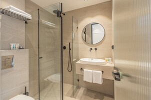 Un baño moderno con ducha de vidrio, espejo redondo, lavamanos y perchero.