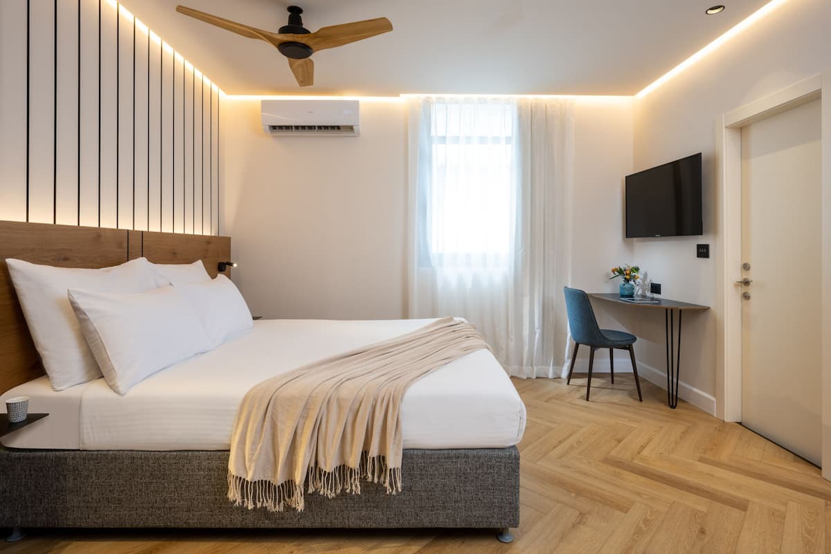 A modern hotel room with a large bed, a desk, a TV, and a ceiling fan.