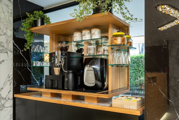 A coffee station with a tea box, coffee makers, and jars of sugar and coffee.