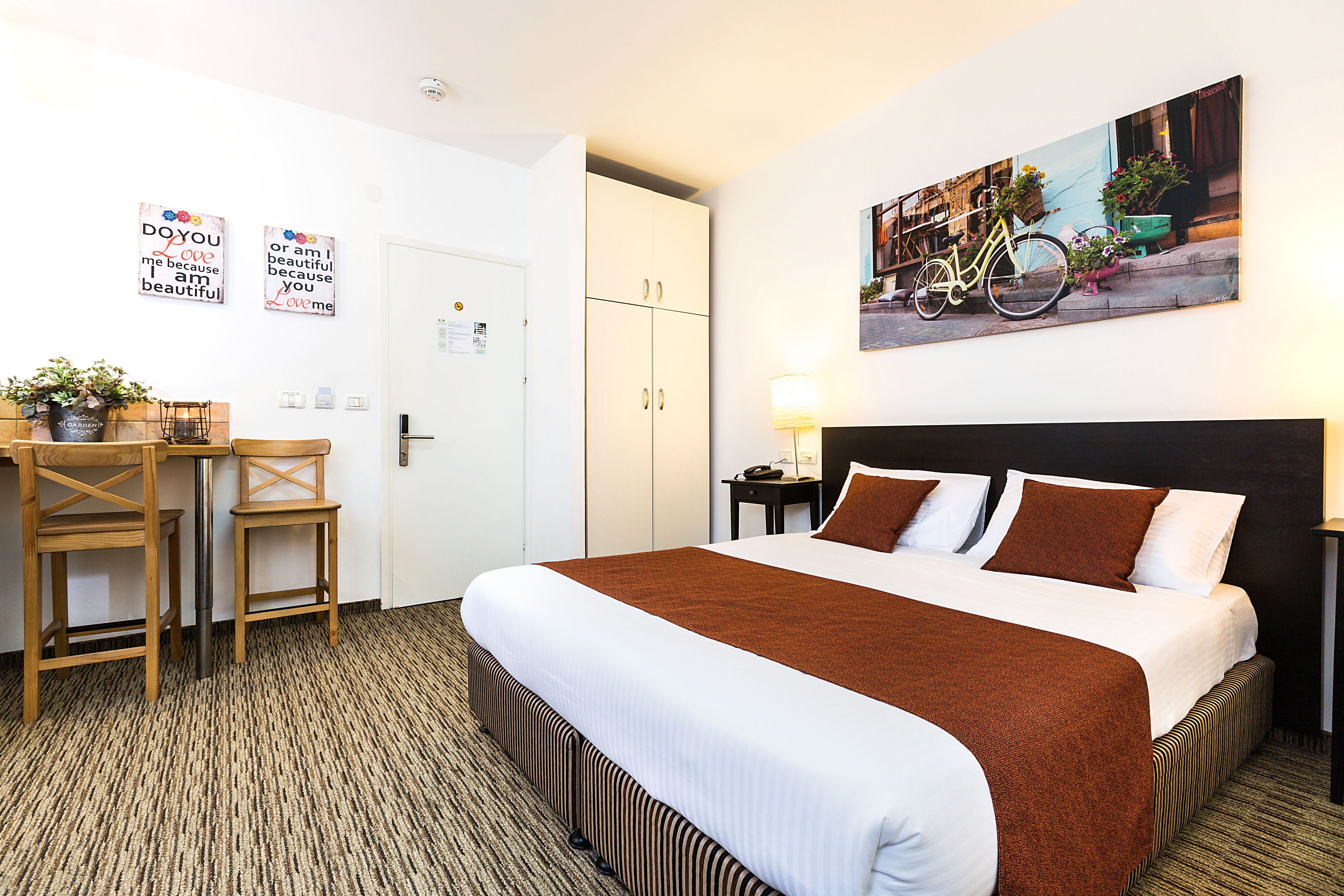 Habitación de hotel con una cama grande, un escritorio con sillas, una planta en maceta y un cuadro colgado en la pared.