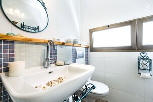 A bathroom with a white sink, a mirror, a toilet, and a window.