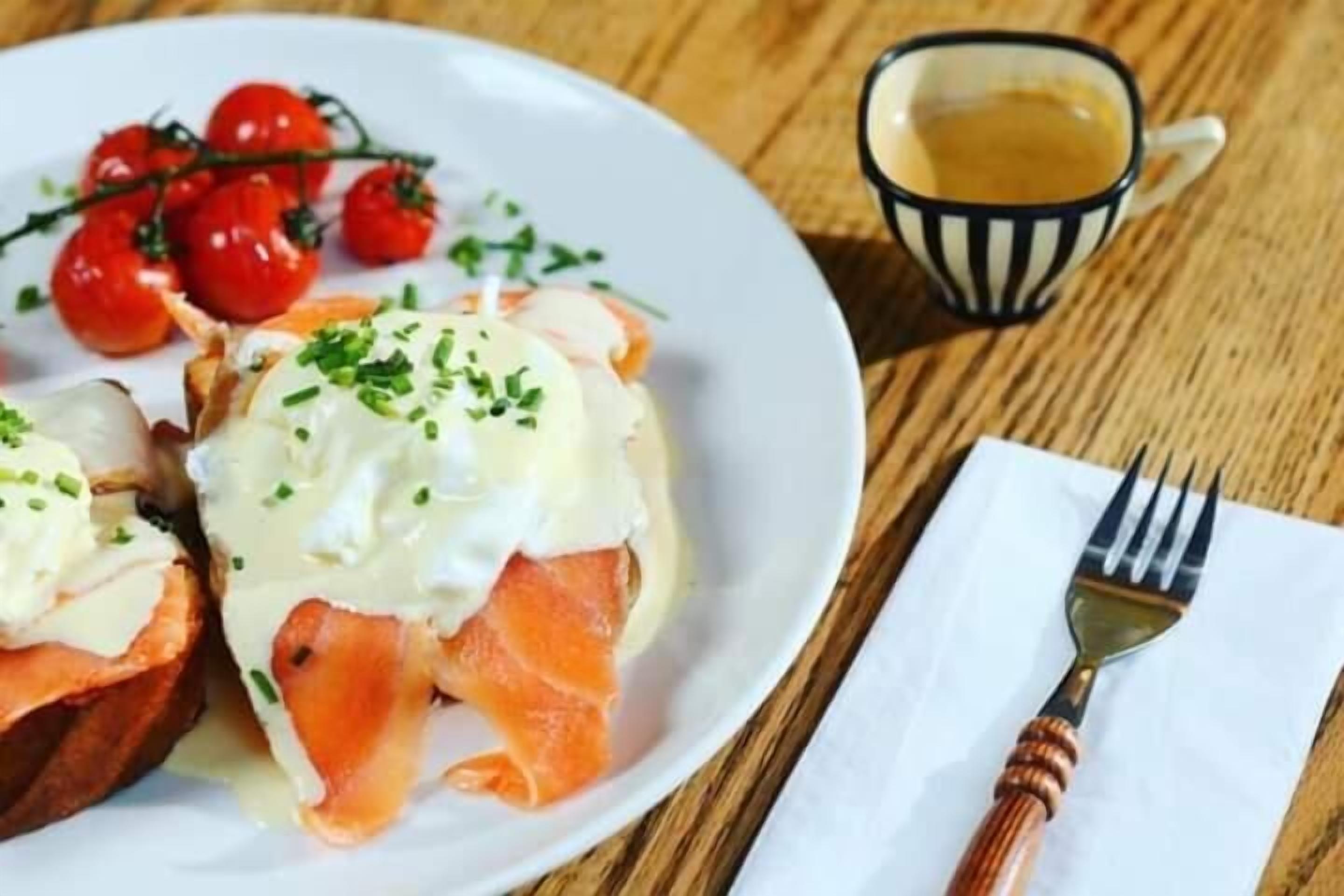 Une assiette de saumon fumé, accompagnée de sauce hollandaise et de tomates cerises, est posée sur une table en bois.