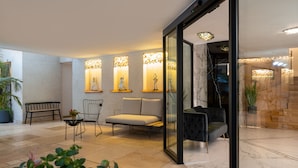 A modern lobby with a seating area, a glass partition, and decorative wall sconces.