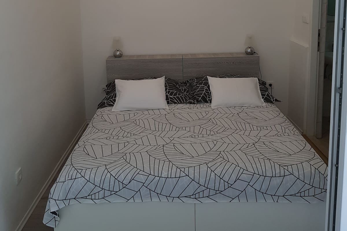 A bedroom with a bed, two framed pictures on the wall, and a door to the right.