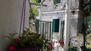 A hanging plant with red flowers, a white wall, and a green gate in a courtyard. - Stipan Studio & Room (Split)