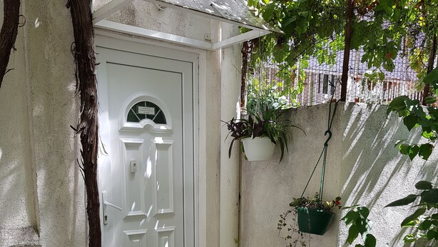 A white door with a small set of steps leading up to it, surrounded by greenery and hanging planters. - Stipan Studio & Room (Split)