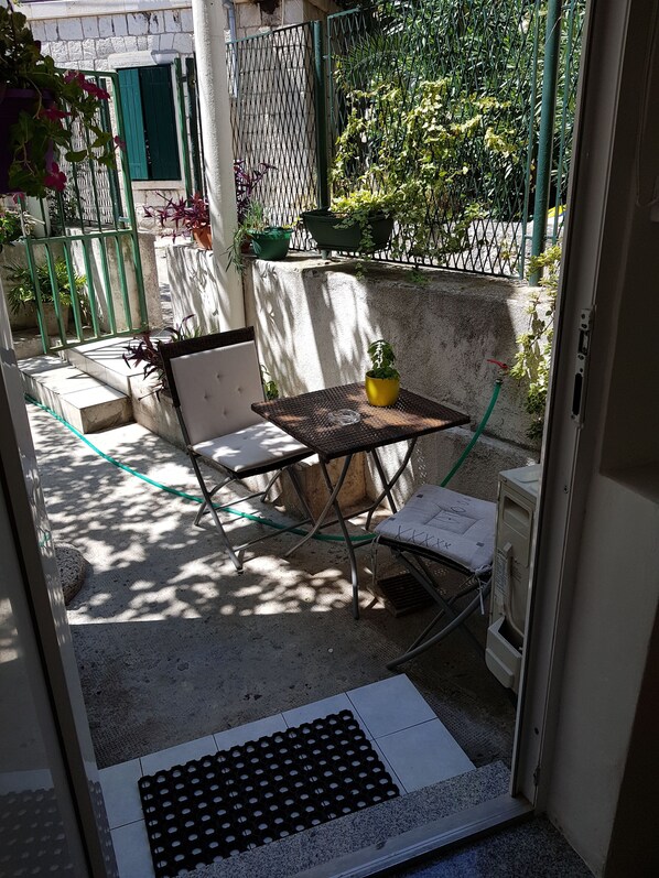 Un petit espace extérieur aménagé avec une table et des chaises, entouré d’un mur en béton et d’une clôture métallique.