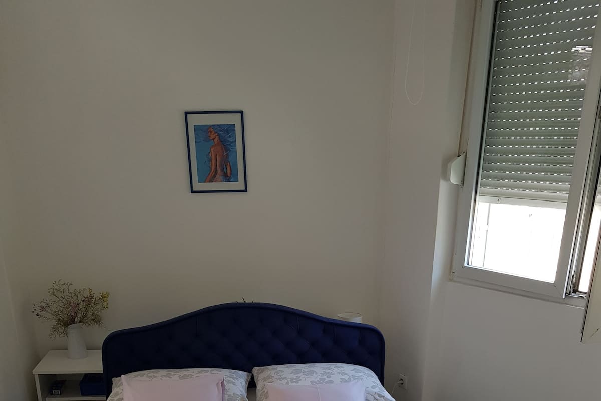 A neatly made bed with floral bedding, a dark headboard, and a small bedside table with a vase.