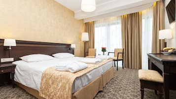 A hotel room with a large bed, two bedside tables, a desk, and a chair.