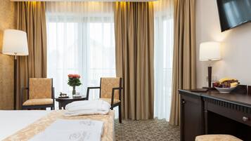 A hotel room with a bed, two chairs, a desk, a TV, and a fruit bowl.