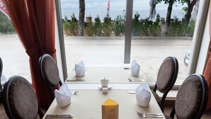 Een tafel voor vier met een menukaart in het midden, uitzicht op strand en zee door grote ramen, en een vlag op de achtergrond.