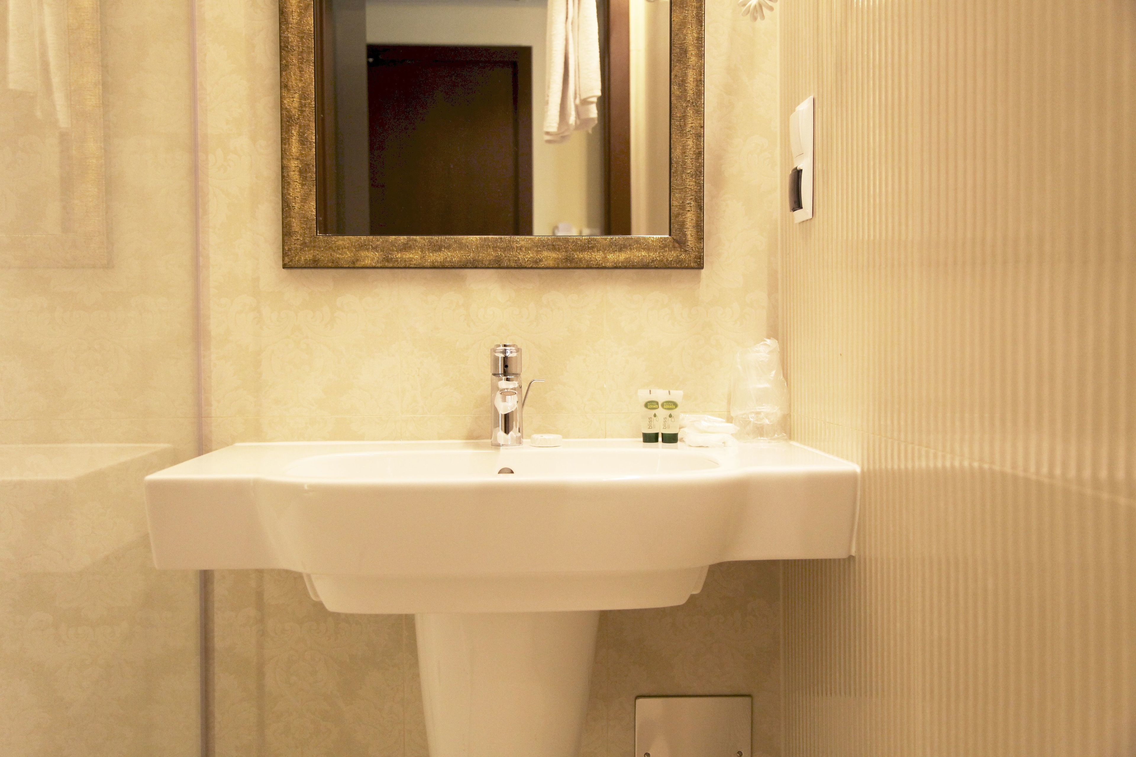 A bathroom with a white sink, a mirror with a gold frame, and a towel hanging on the wall.