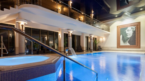 Een modern binnenzwembad met glazen balustrade, een bubbelbad en een trap naar een tweede verdieping.