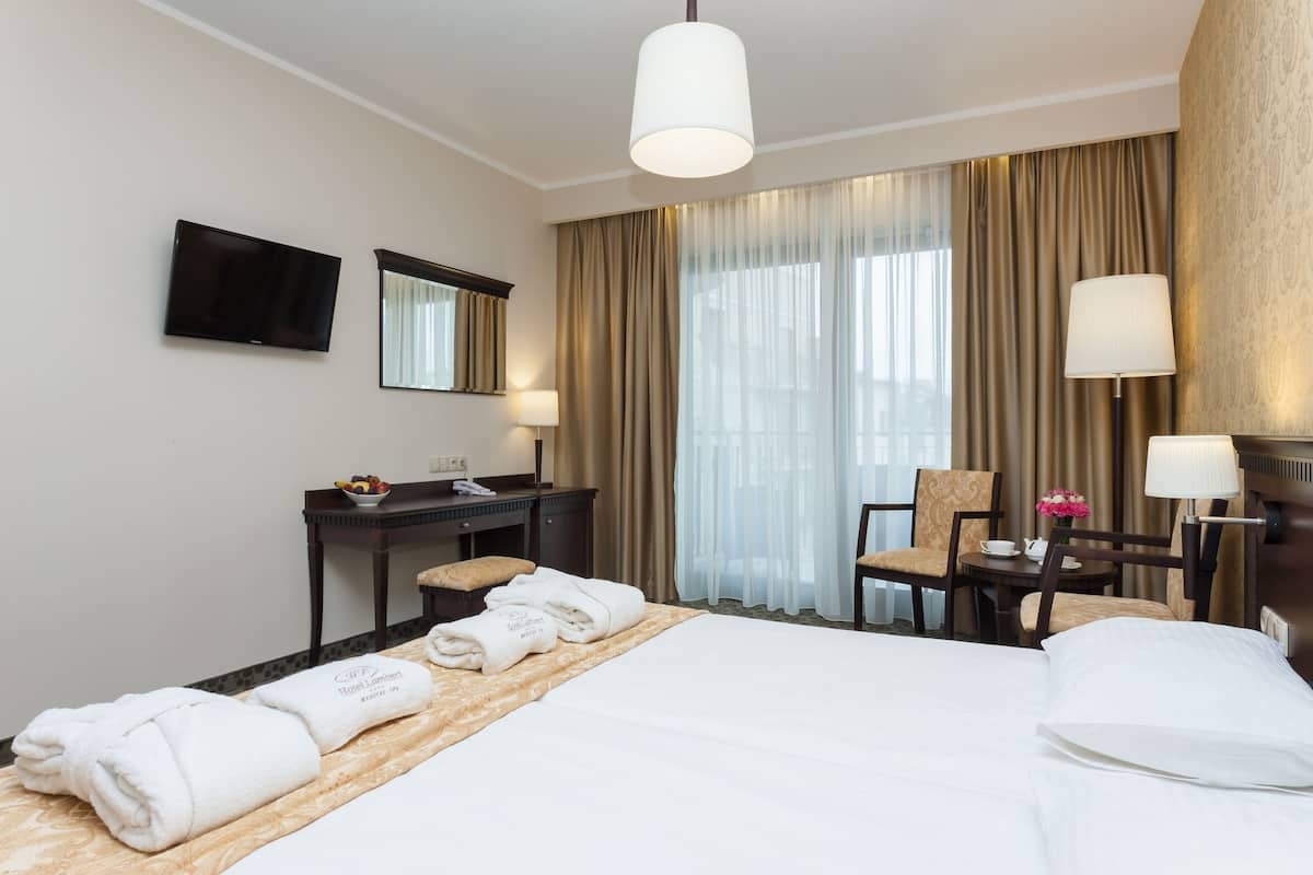 Una habitación de hotel con cama, escritorio, silla, televisor y ventana con cortinas.
