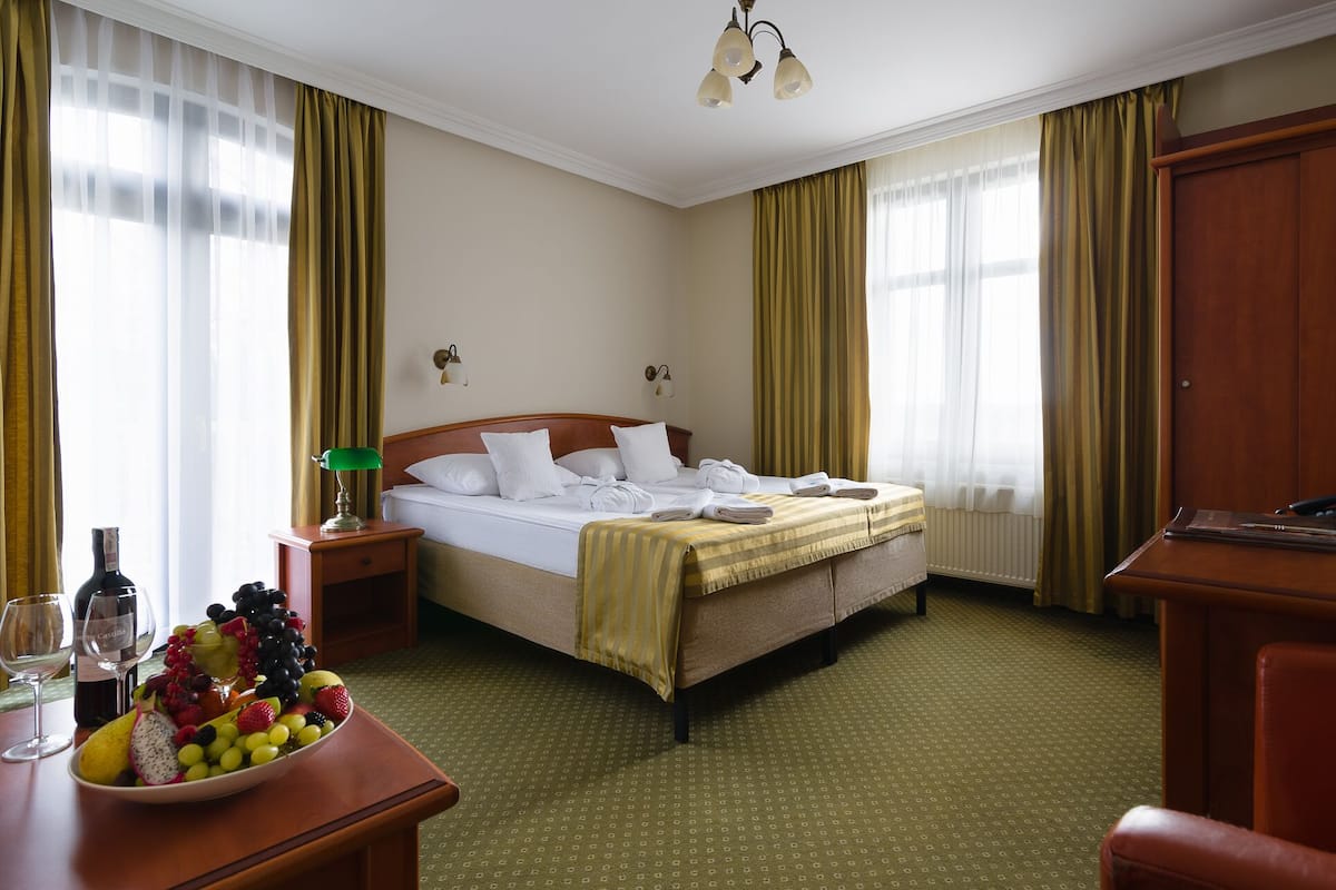 Habitación de hotel con cama, escritorio con silla, frutero y botella de vino.