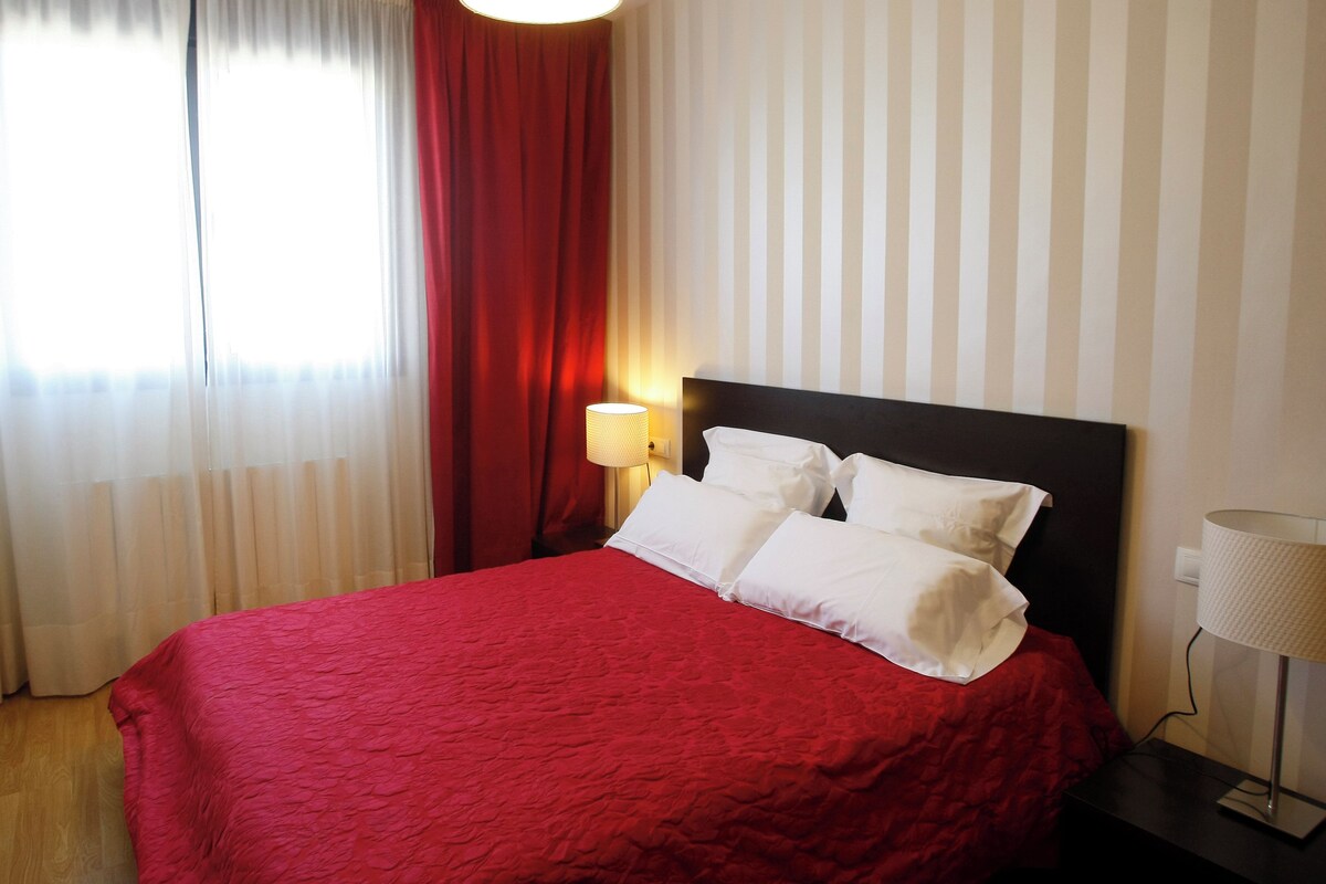 Habitación de hotel con una cama, una mesita de noche, una lámpara y una ventana con cortinas.