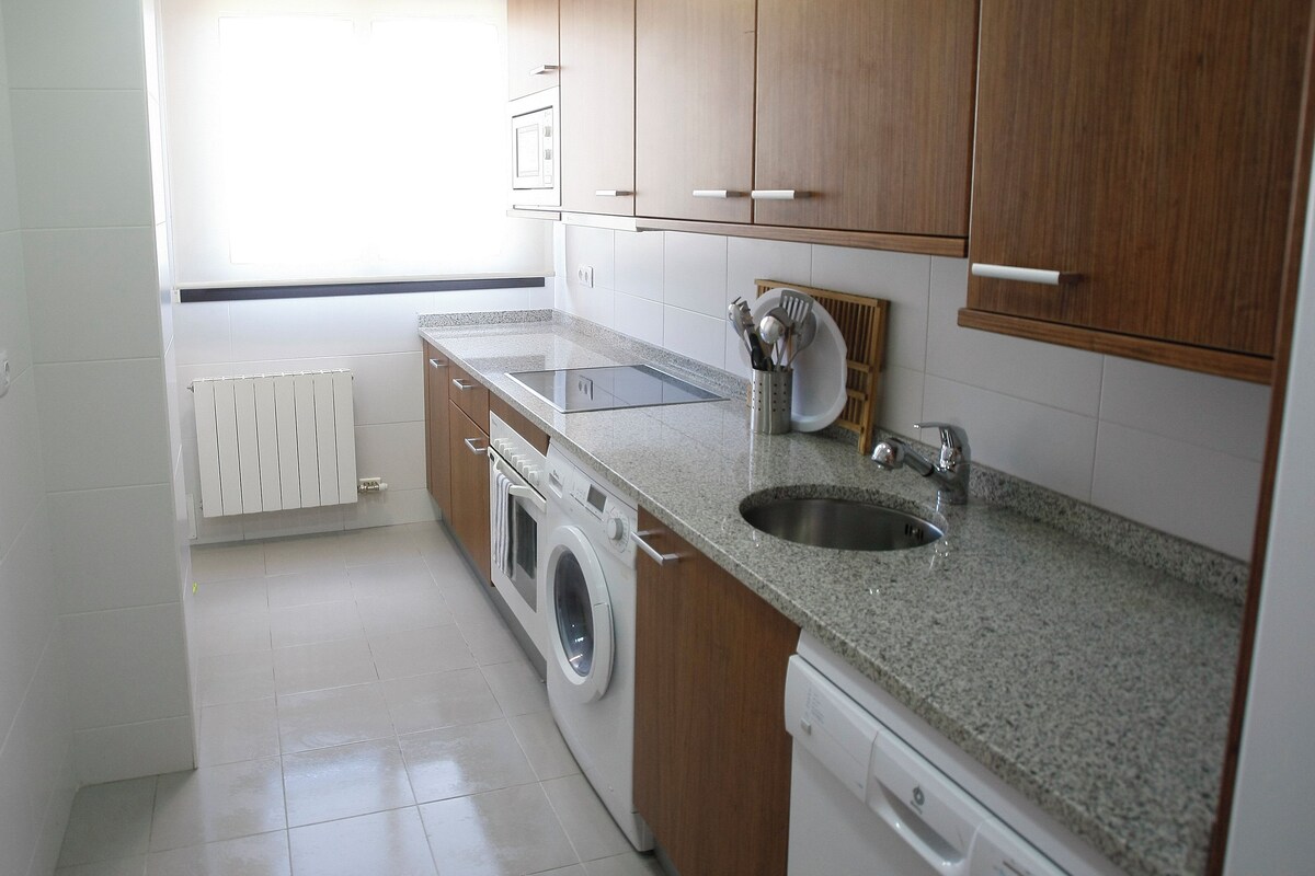 A compact kitchen with a washing machine, a sink, and wooden cabinets.