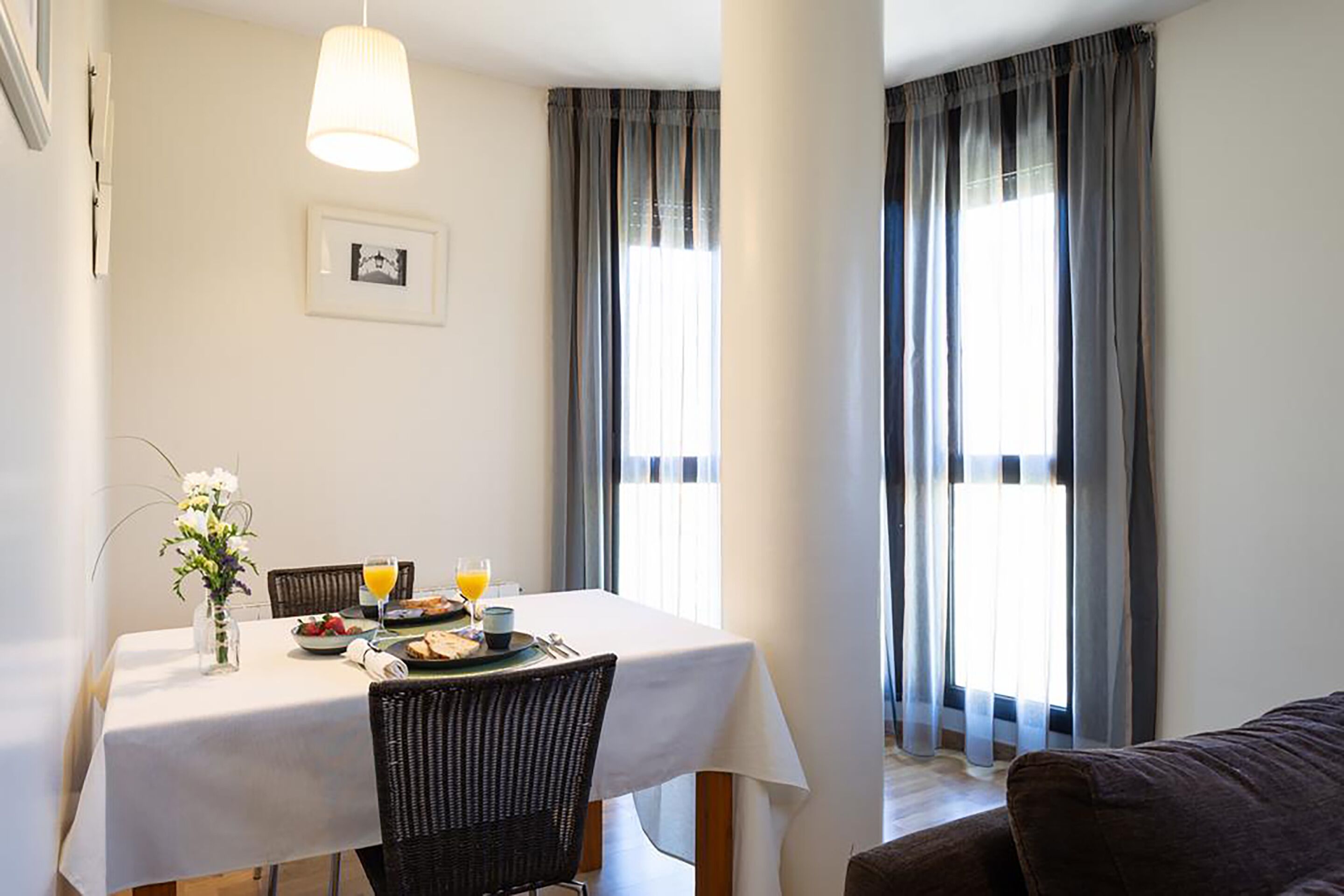 A dining area with a table set for breakfast, including a vase of flowers, a plate of food, and a glass of orange juice.