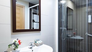 Un baño con lavamanos blanco, un espejo y zona de ducha con paredes de azulejos.