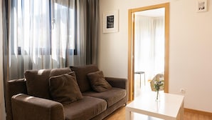 Una sala de estar con un sofá marrón, una mesa blanca y un ventanal con cortinas.