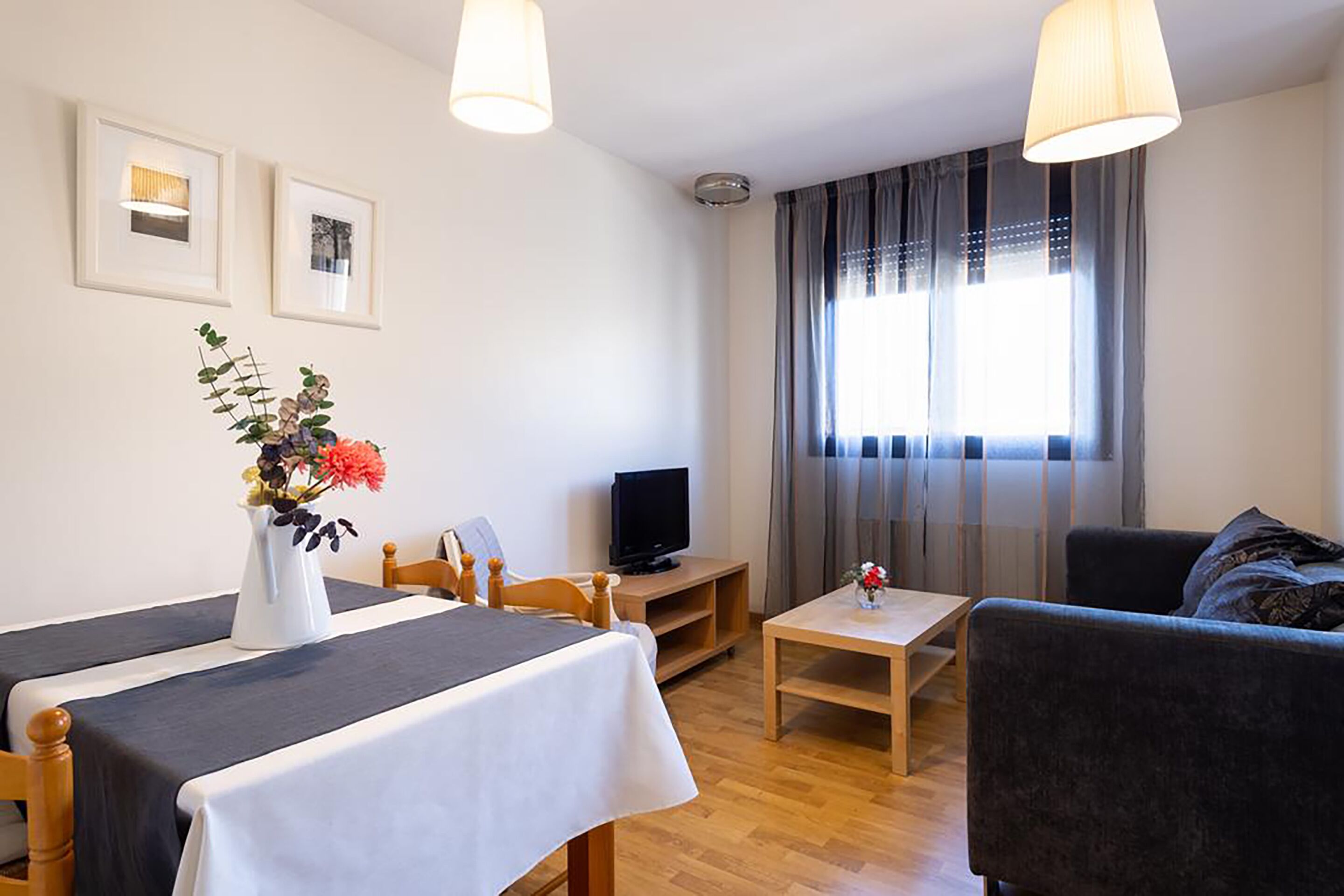 Une chambre d’hôtel avec un lit, une télévision, une petite table ornée d’un vase de fleurs et un canapé.