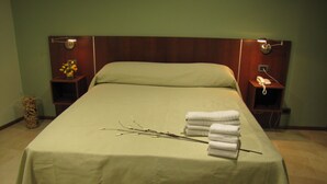 A neatly made bed with a green bedspread, a stack of white towels, and a vase with yellow flowers on a bedside table. - Tunkelén Apart Hotel (Mendoza)