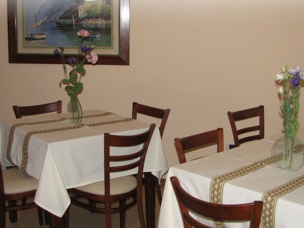 A dining area with tables covered in white tablecloths, wooden chairs, and vases with flowers.