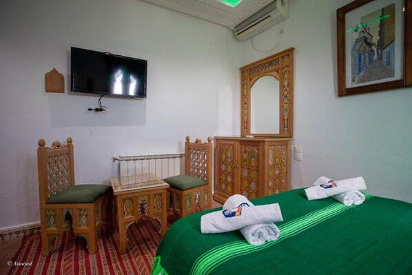 Habitación de hotel con una colcha verde, muebles de madera, un televisor de pantalla plana y un cuadro en la pared.