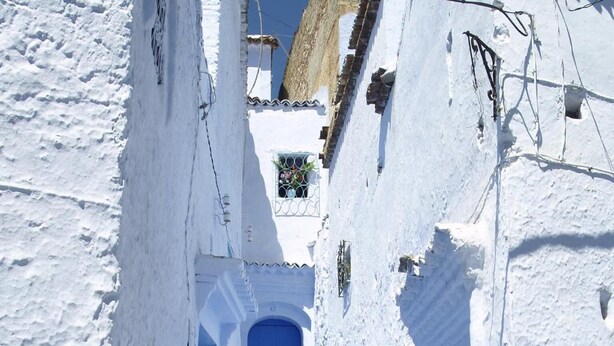 Un callejón estrecho cubierto de nieve, con edificios blancos y una puerta azul al final.