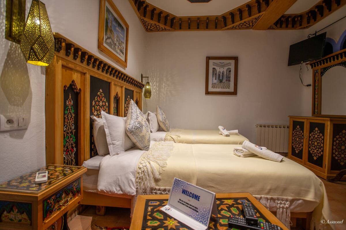 A hotel room with two beds, a laptop on a side table, a TV, and decorative elements.