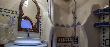 A bathroom with a sink, a mirror with a decorative frame, a shower, and patterned tiles.
