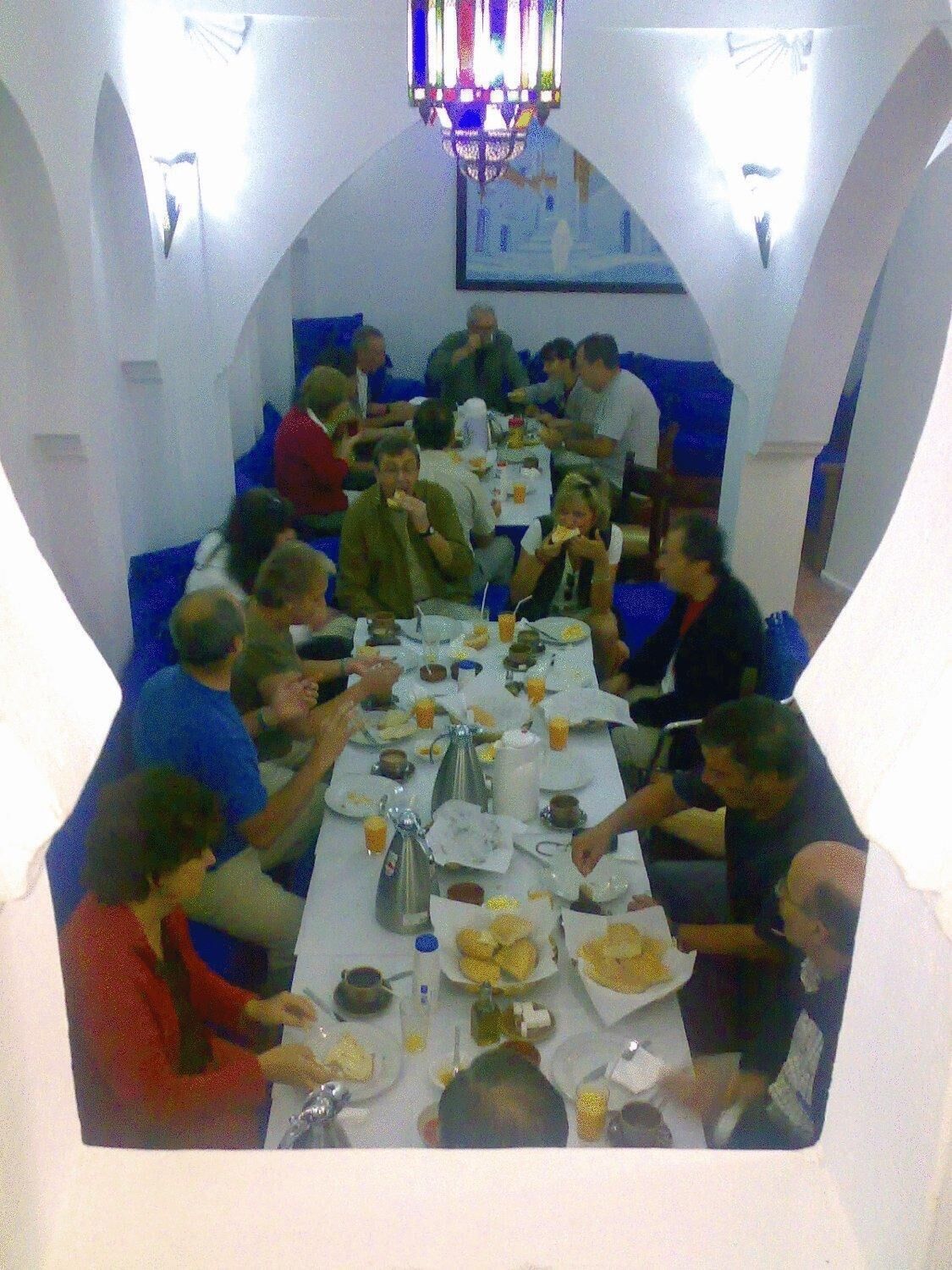 Un espace repas avec une longue table, des personnes assises et divers plats et boissons.