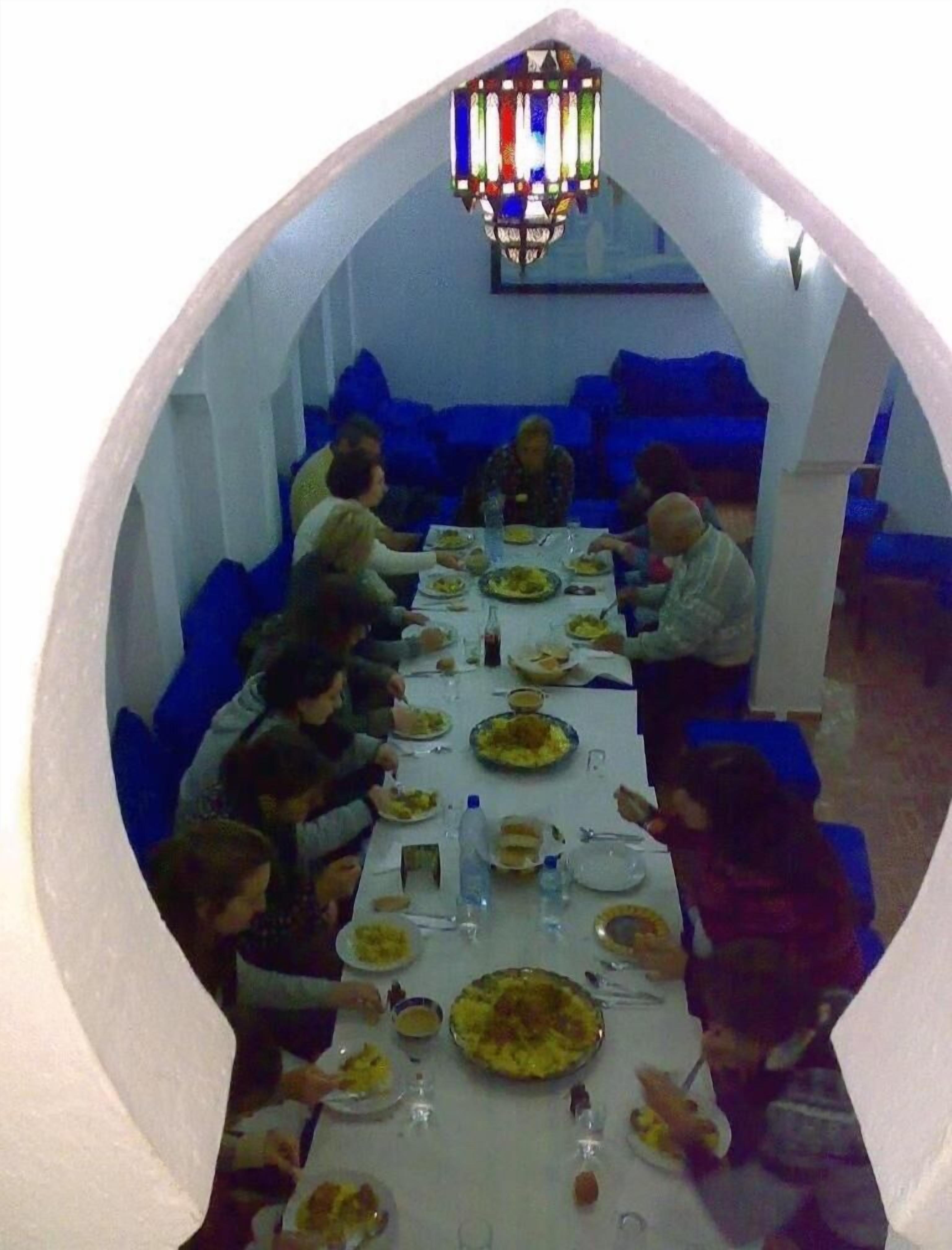 Un comedor con una mesa larga, asientos acolchados azules y una lámpara con vidrieras.