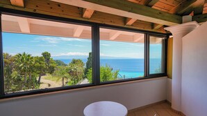 A room with a large window overlooking a coastal landscape, a small round table, and two chairs.