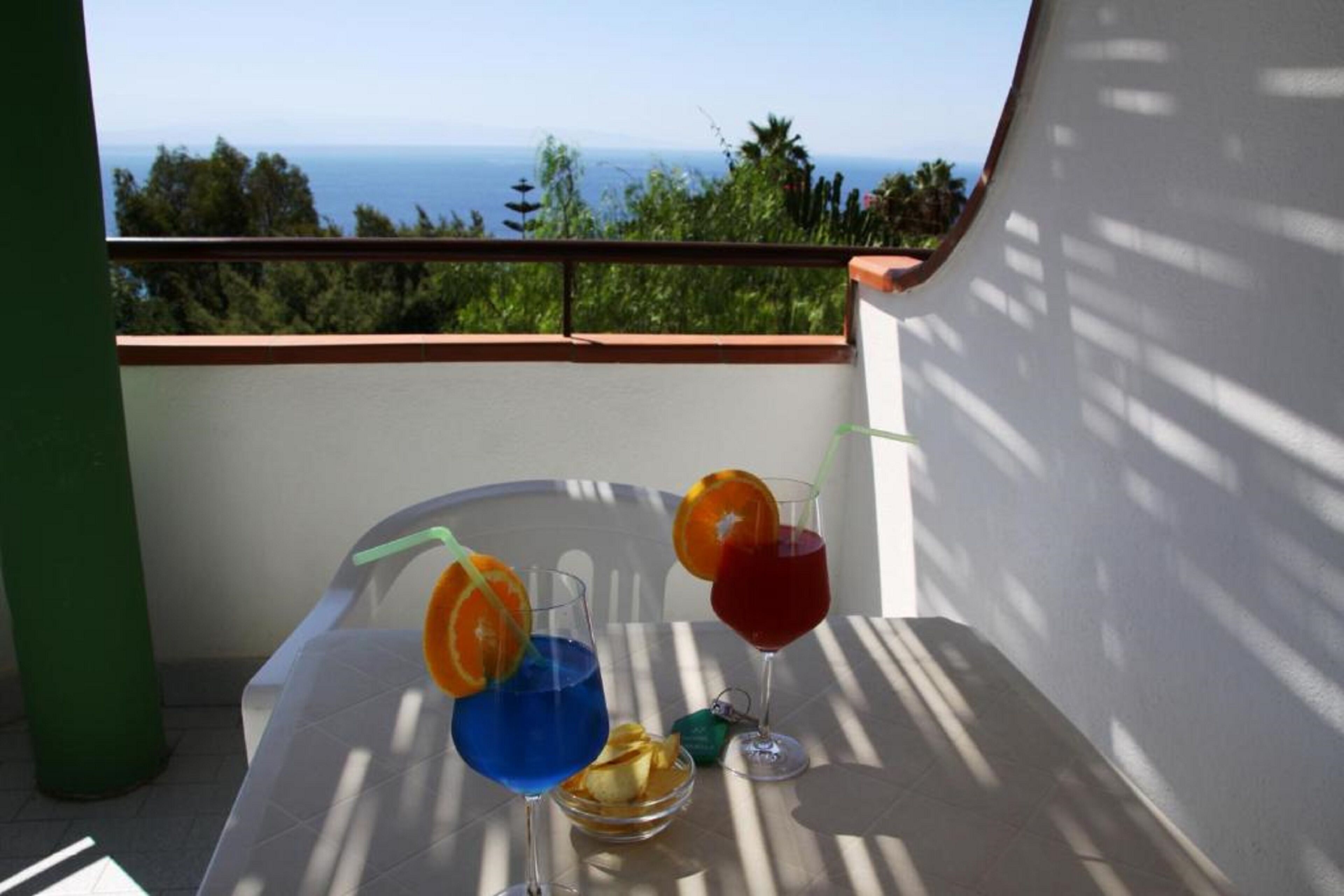 En balkon med et bord dækket til drinks, havudsigt og en grøn søjle.