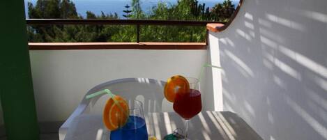 En balkon med et bord dækket til drinks, havudsigt og en grøn søjle.
