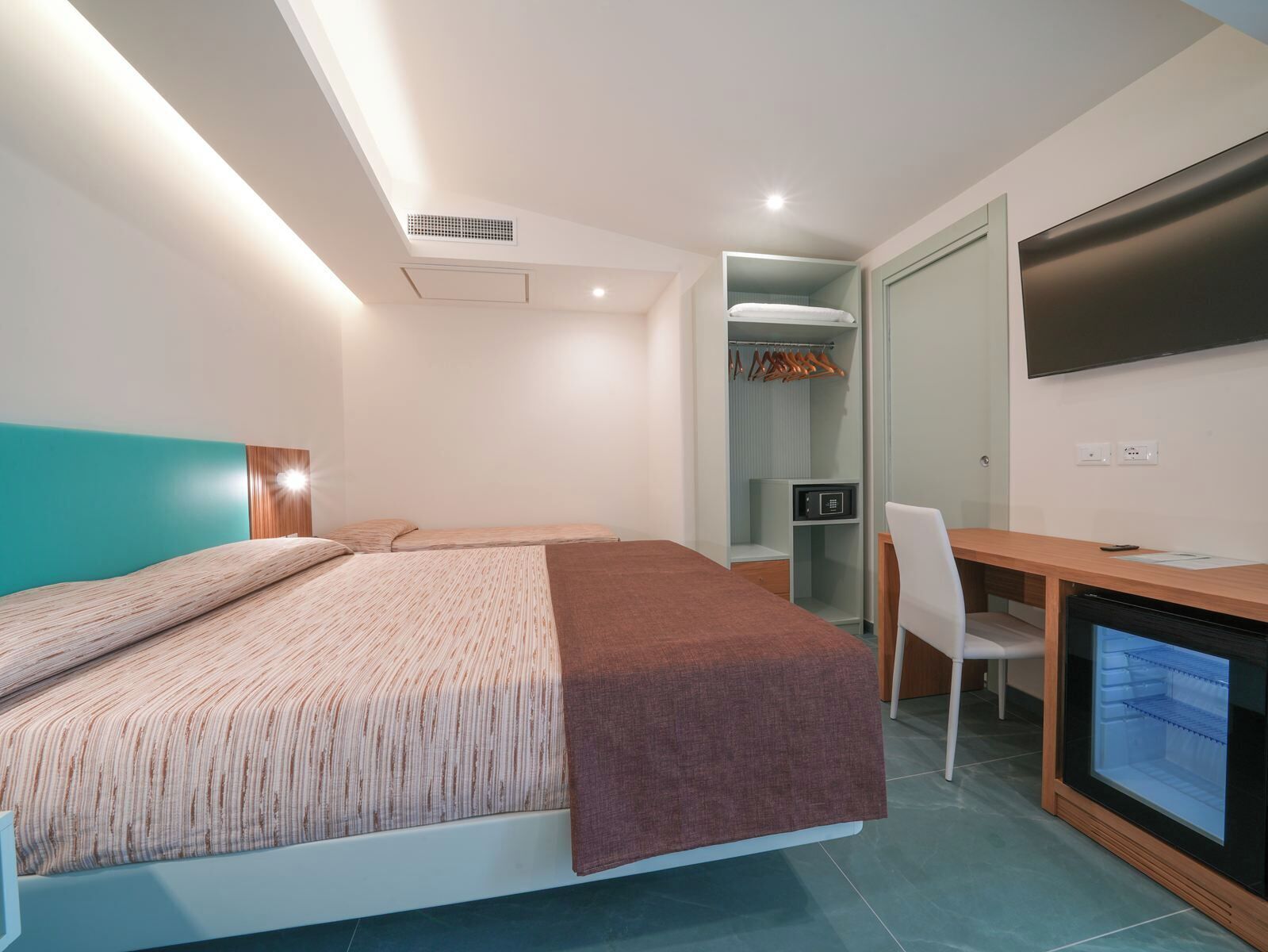 Une chambre moderne comprenant un lit, un bureau, une chaise, une télévision et un dressing.