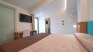 A modern hotel room with a large bed, a desk, a TV mounted on the wall, and a window with curtains.