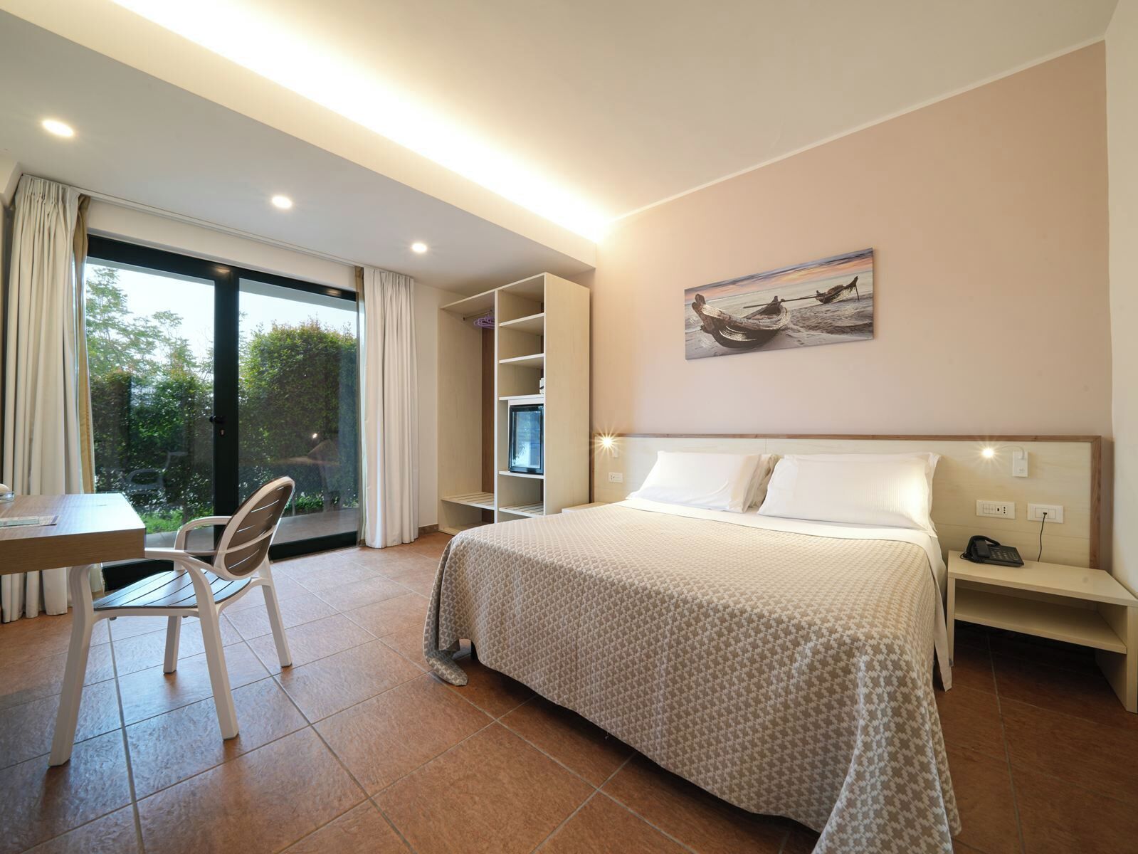 Une chambre d’hôtel avec un lit, un bureau, une chaise, une armoire et une fenêtre avec des rideaux.