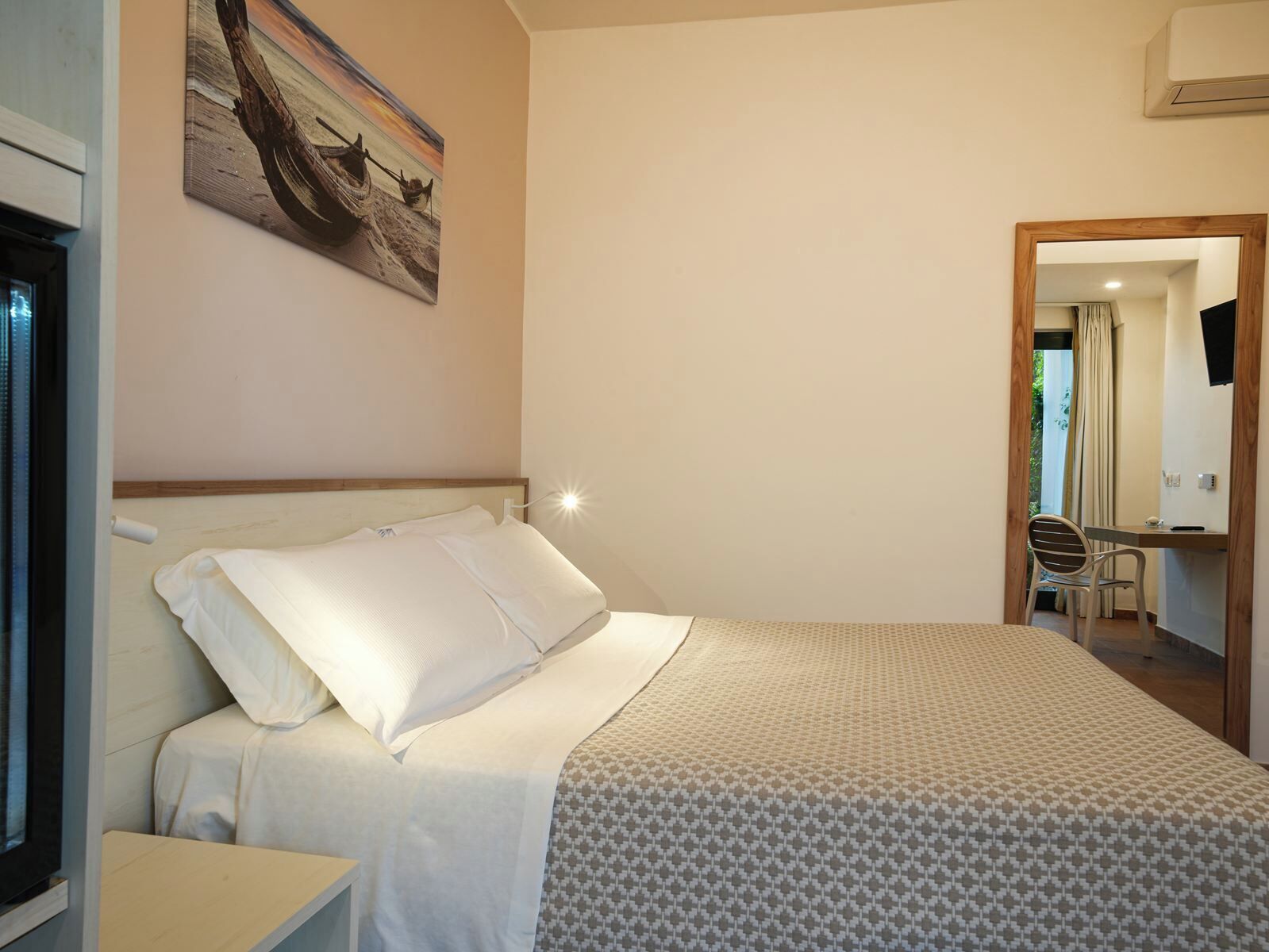 A neatly made bed with a patterned bedspread, a bedside table, and a wall-mounted painting.