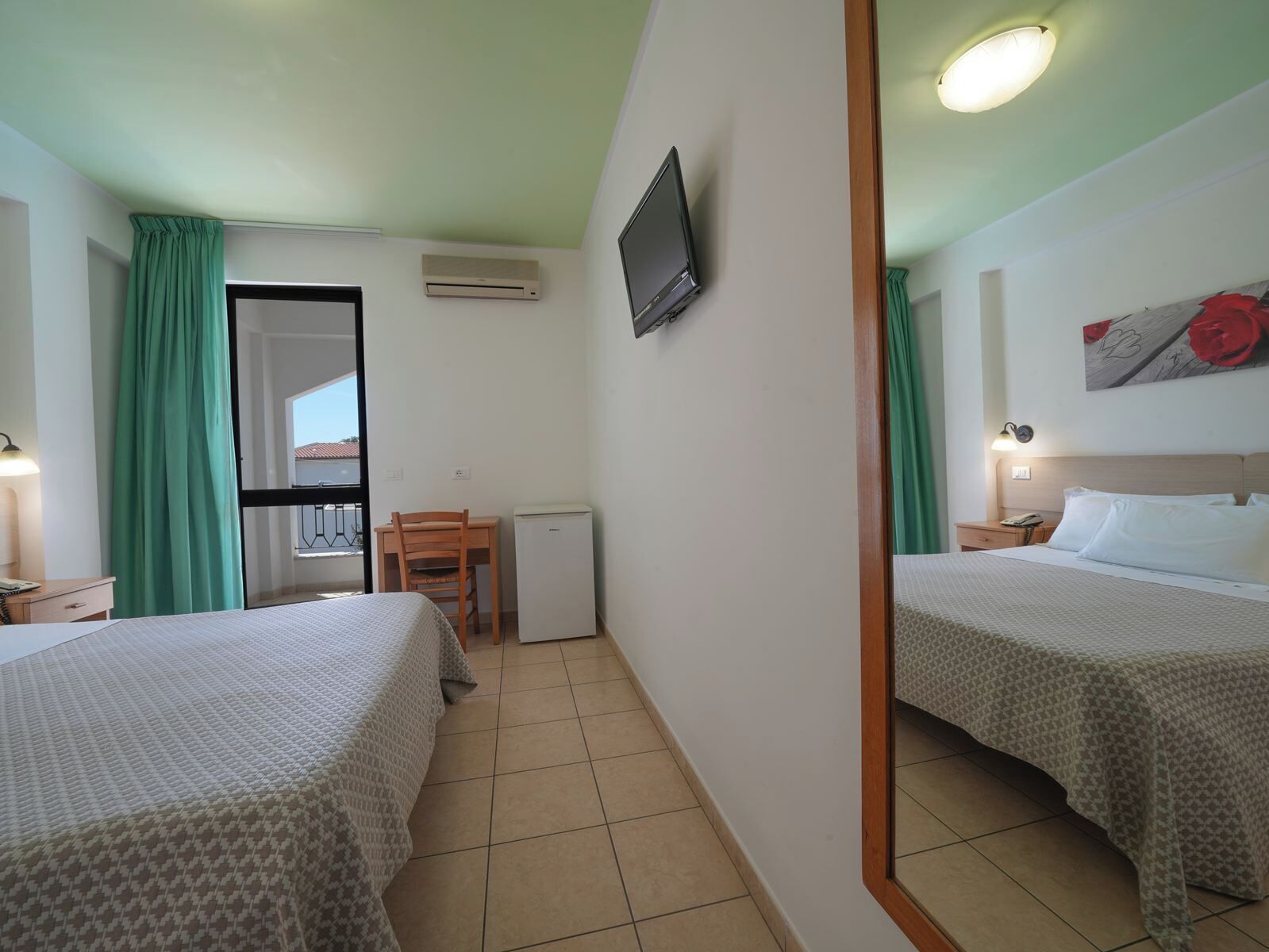 A hotel room with two beds, a small desk, a television, and a window with curtains.