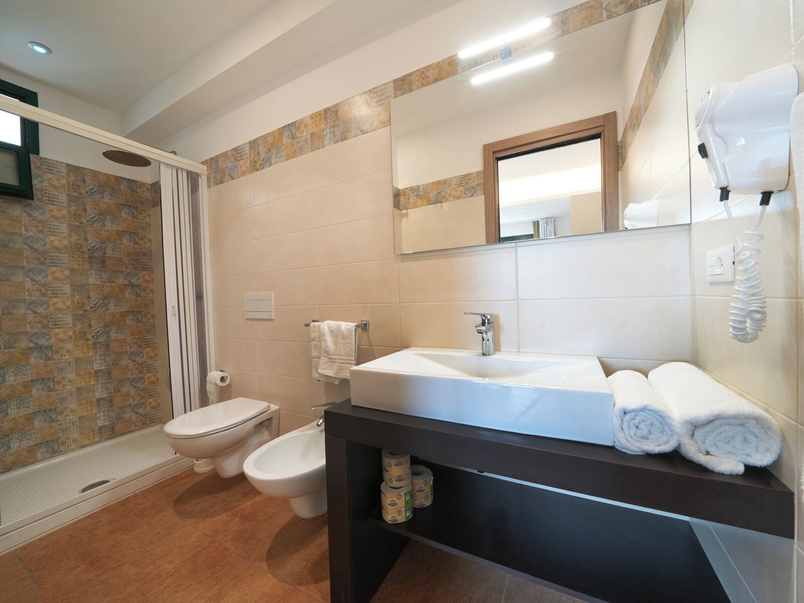 Une salle de bain moderne équipée d’une douche, de toilettes, d’un bidet et d’un meuble-lavabo avec un évier et un porte-serviettes.