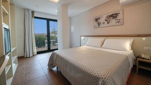 A hotel room with a large bed, a view through a sliding door to an outdoor area, a world map on the wall, and an air conditioning unit.