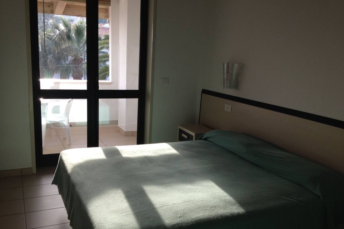 A room with a bed, a nightstand, and a window.