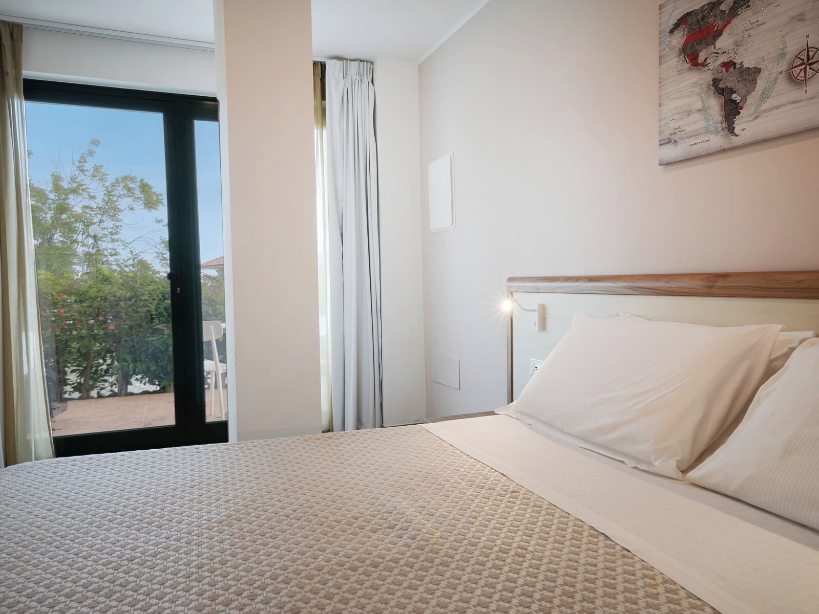 A hotel room with a bed, a window, and a wall-mounted map.