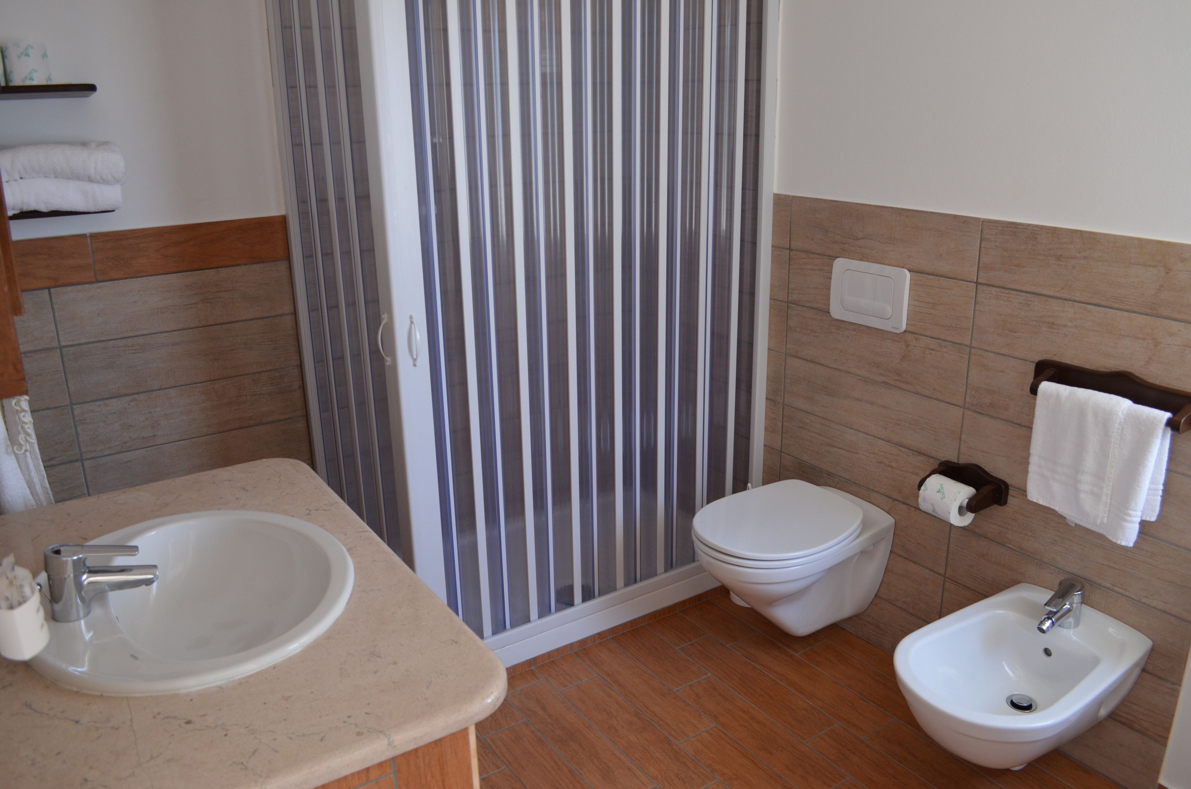 A bathroom with a sink, toilet, bidet, and striped shower curtain.
