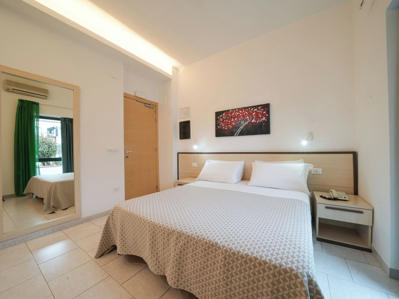 Habitación de hotel con una cama grande, una mesita de noche con teléfono, un espejo y un cuadro en la pared.