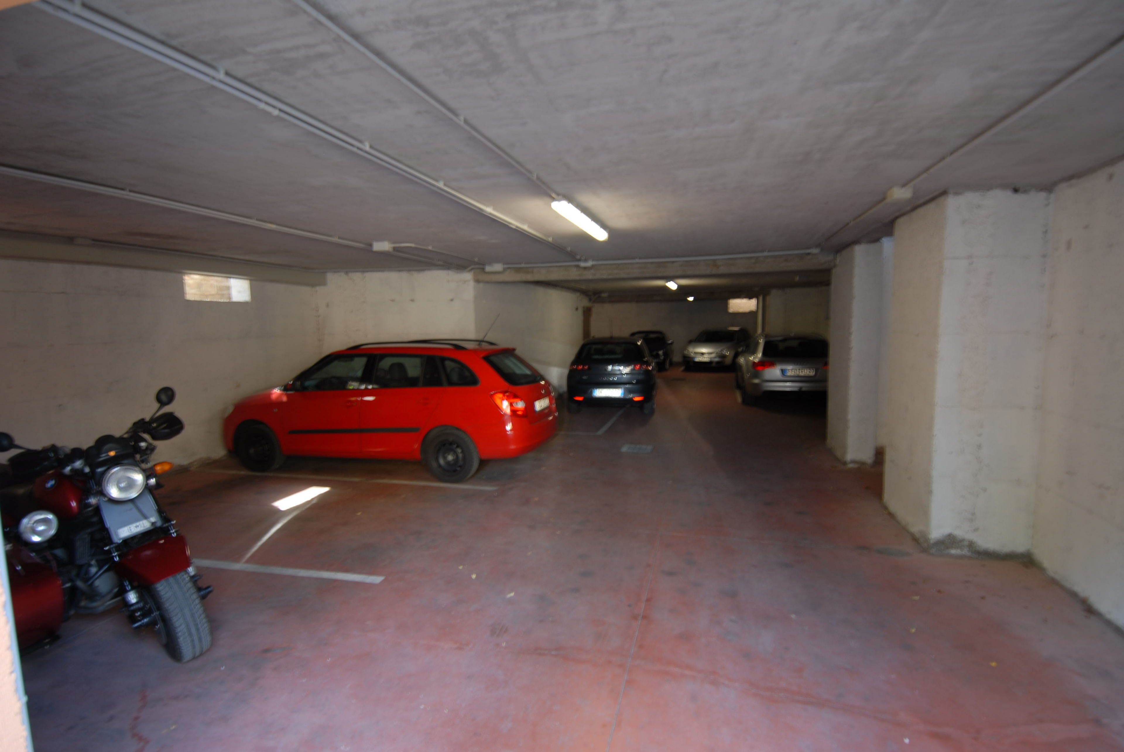 A parking garage with several cars and a motorcycle.